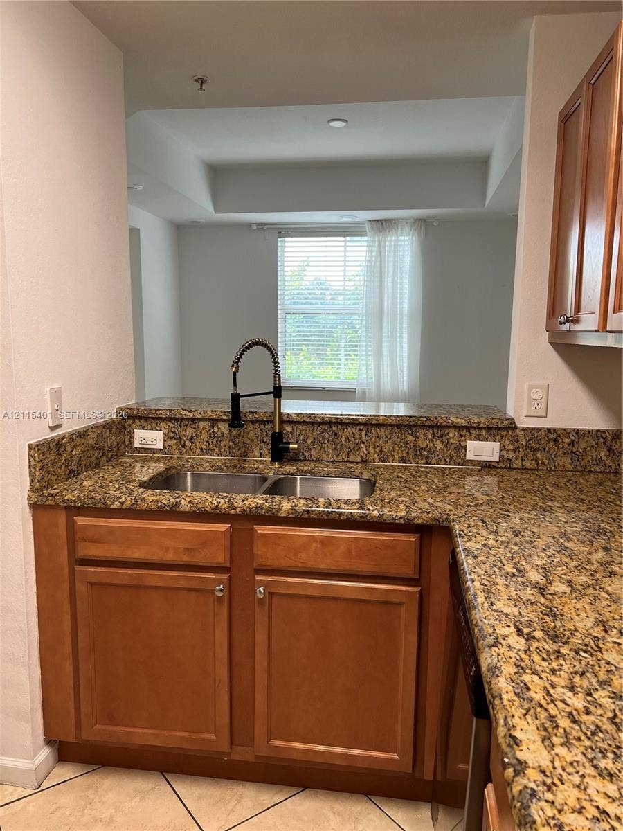 11503 NW 89th Street, #104, Doral, Doral, FL 33178 Kitchen featuring stone countertops, wood-finish cabinetry, a dual-basin stainless steel sink with a high-arch pull-down faucet, and tiled flooring