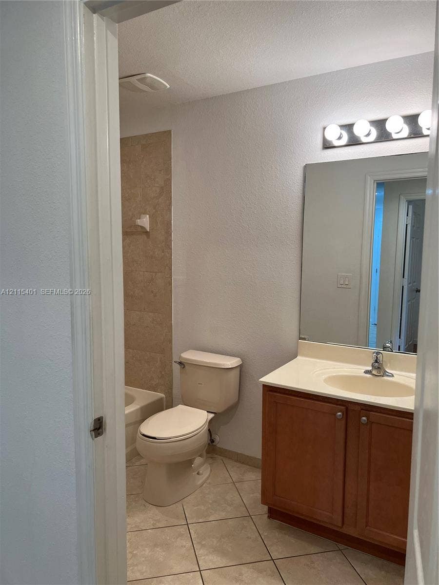 11503 NW 89th Street, #104, Doral, Doral, FL 33178 Bathroom featuring a wood-finish vanity with a molded countertop, a large wall-mounted mirror, ceramic tile flooring, and a tub enclosure with stone-style wall tile