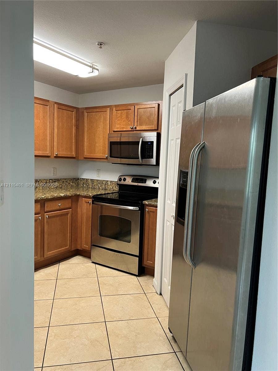 11503 NW 89th Street, #104, Doral, Doral, FL 33178 Kitchen featuring wood cabinetry, stone-finish countertops, stainless steel appliances, and tile flooring