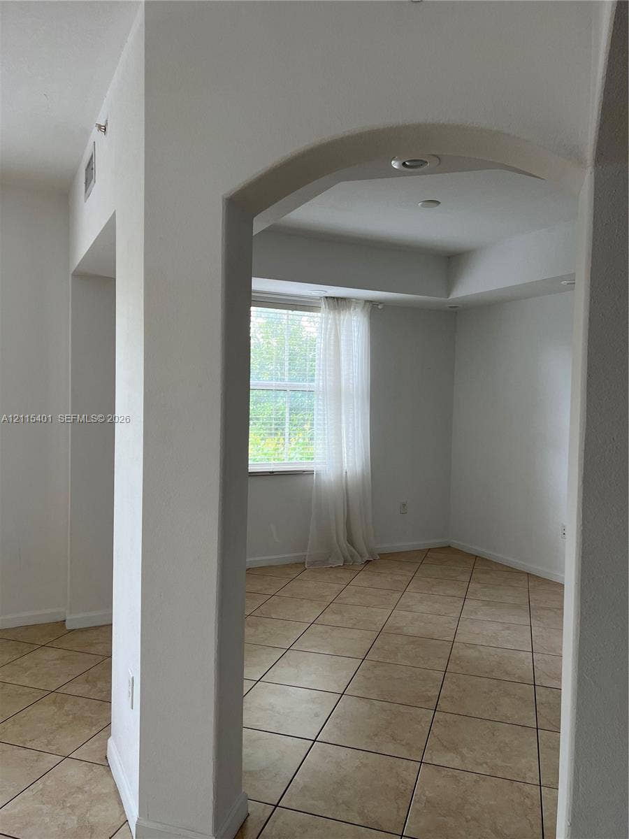 11503 NW 89th Street, #104, Doral, Doral, FL 33178 Arched entryway featuring neutral-toned tile flooring, recessed ceiling lighting, and a tray ceiling detail