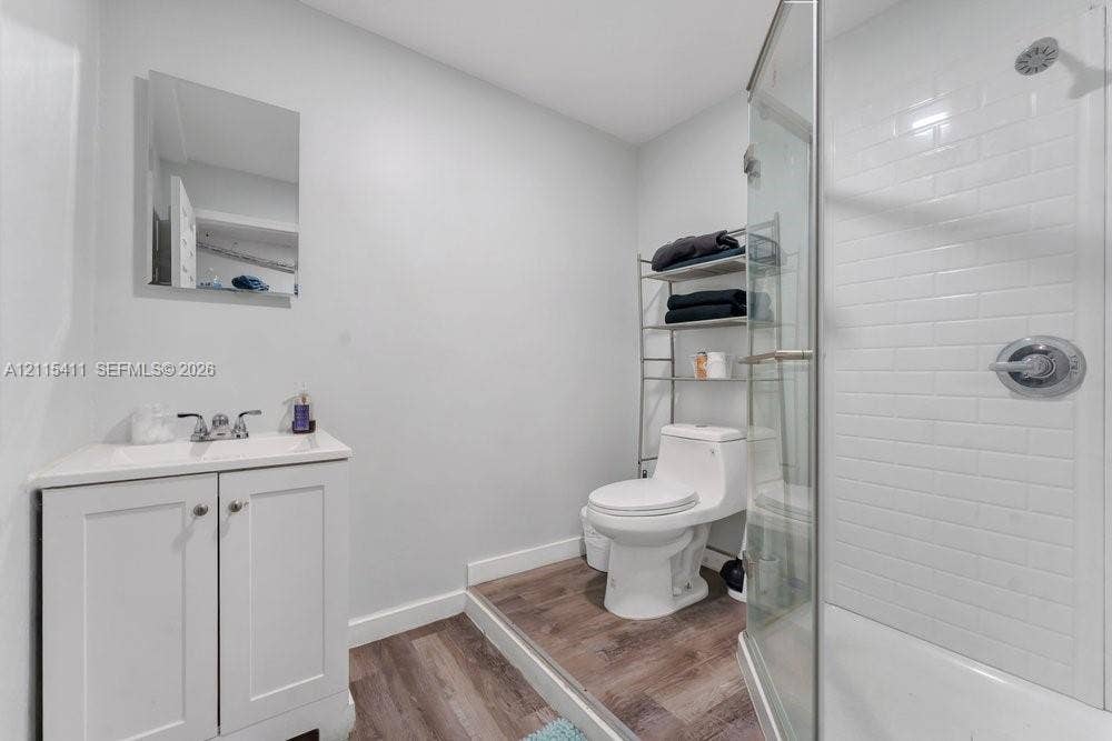 20302 NW 39th Court, Miami Gardens, FL 33055 Bathroom featuring a white vanity cabinet with an integrated sink, wood-finish flooring, a toilet, and a glass-enclosed shower with white subway tile surround