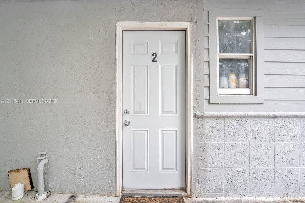 20302 NW 39th Court, Miami Gardens, FL 33055 Exterior entry featuring a six-panel door, textured stucco wall finish, horizontal siding, and a square-pane window with masonry wainscoting
