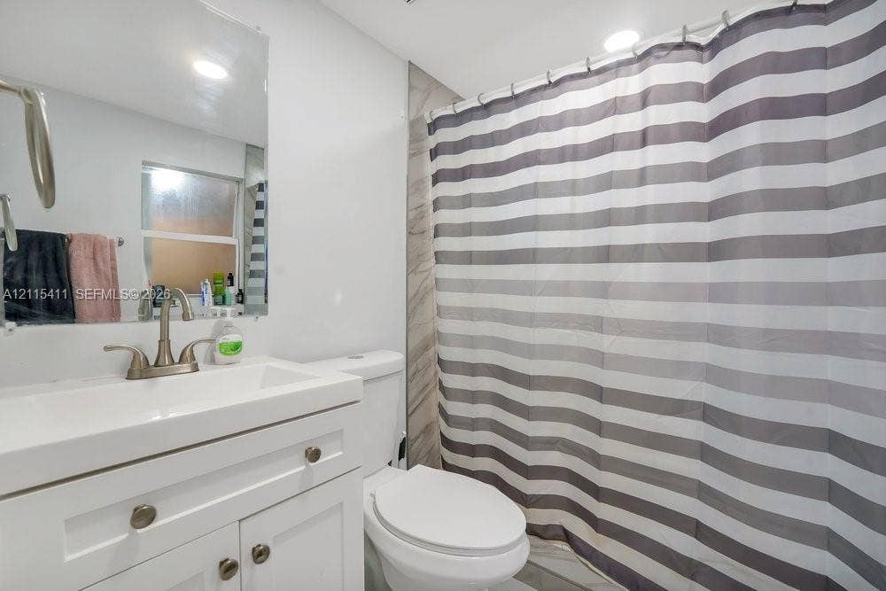 20302 NW 39th Court, Miami Gardens, FL 33055 Bathroom featuring a white vanity cabinet with a rectangular basin, brushed-nickel faucet, large wall-mounted mirror, and tile shower surround