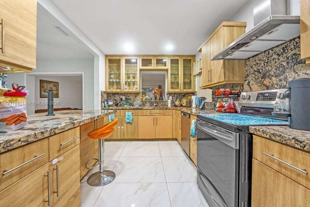 20302 NW 39th Court, Miami Gardens, FL 33055 Kitchen featuring light wood cabinetry, stone countertops, stone tile backsplash, stainless steel range hood, and large-format tile flooring