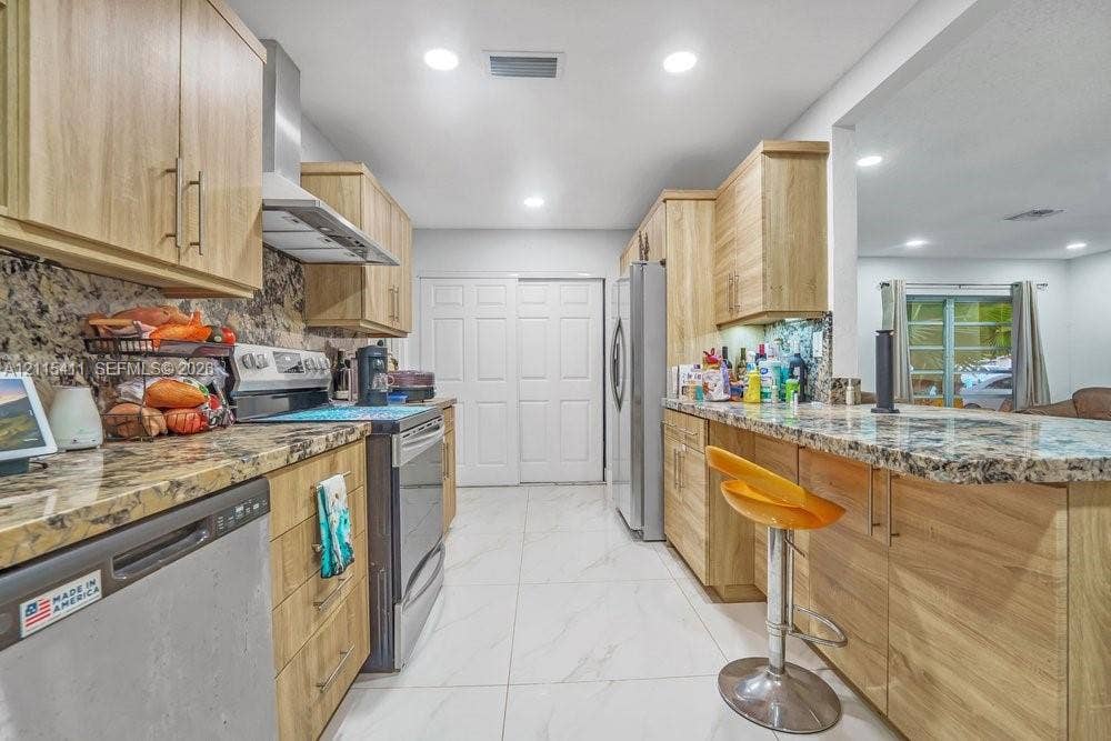 20302 NW 39th Court, Miami Gardens, FL 33055 Kitchen featuring wood-finish cabinetry, stone-style countertops, stainless steel appliances, and large-format tile flooring