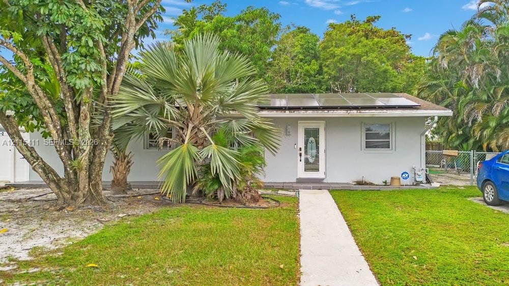 20302 NW 39th Court, Miami Gardens, FL 33055 Single-story exterior featuring a light-toned facade, roof-mounted solar panels, a centered entry door with an oval glass insert, and a concrete walkway leading to the front entrance