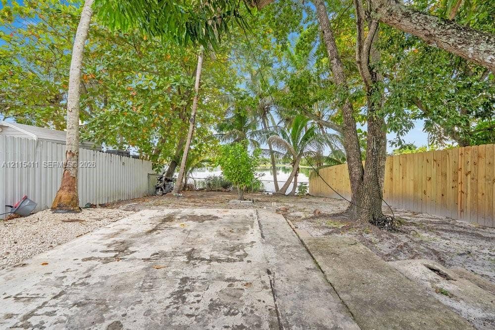 20302 NW 39th Court, Miami Gardens, FL 33055 Outdoor area featuring a concrete slab, mature trees, wood-tone fencing, and corrugated metal privacy screening