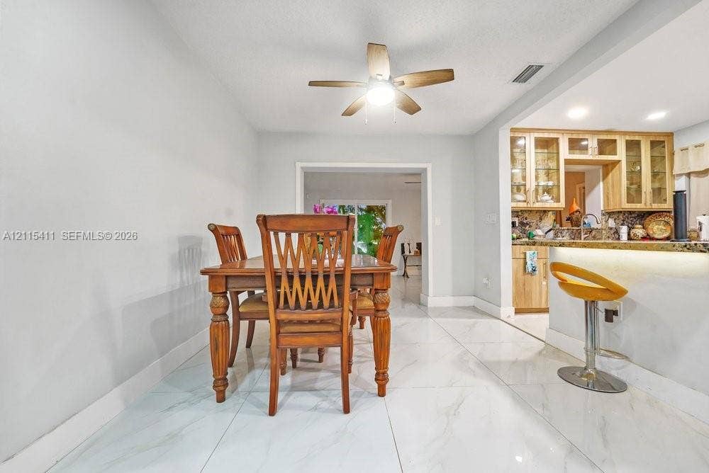 20302 NW 39th Court, Miami Gardens, FL 33055 Dining area featuring large-format tile flooring, a ceiling-mounted fan with integrated lighting, and a kitchen pass-through with under-counter lighting and wood-finish cabinetry