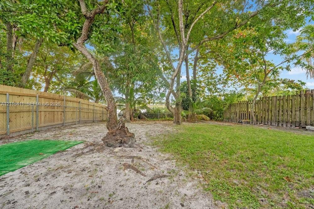 20302 NW 39th Court, Miami Gardens, FL 33055 Backyard featuring a grass lawn, mature trees, and wood-panel fencing