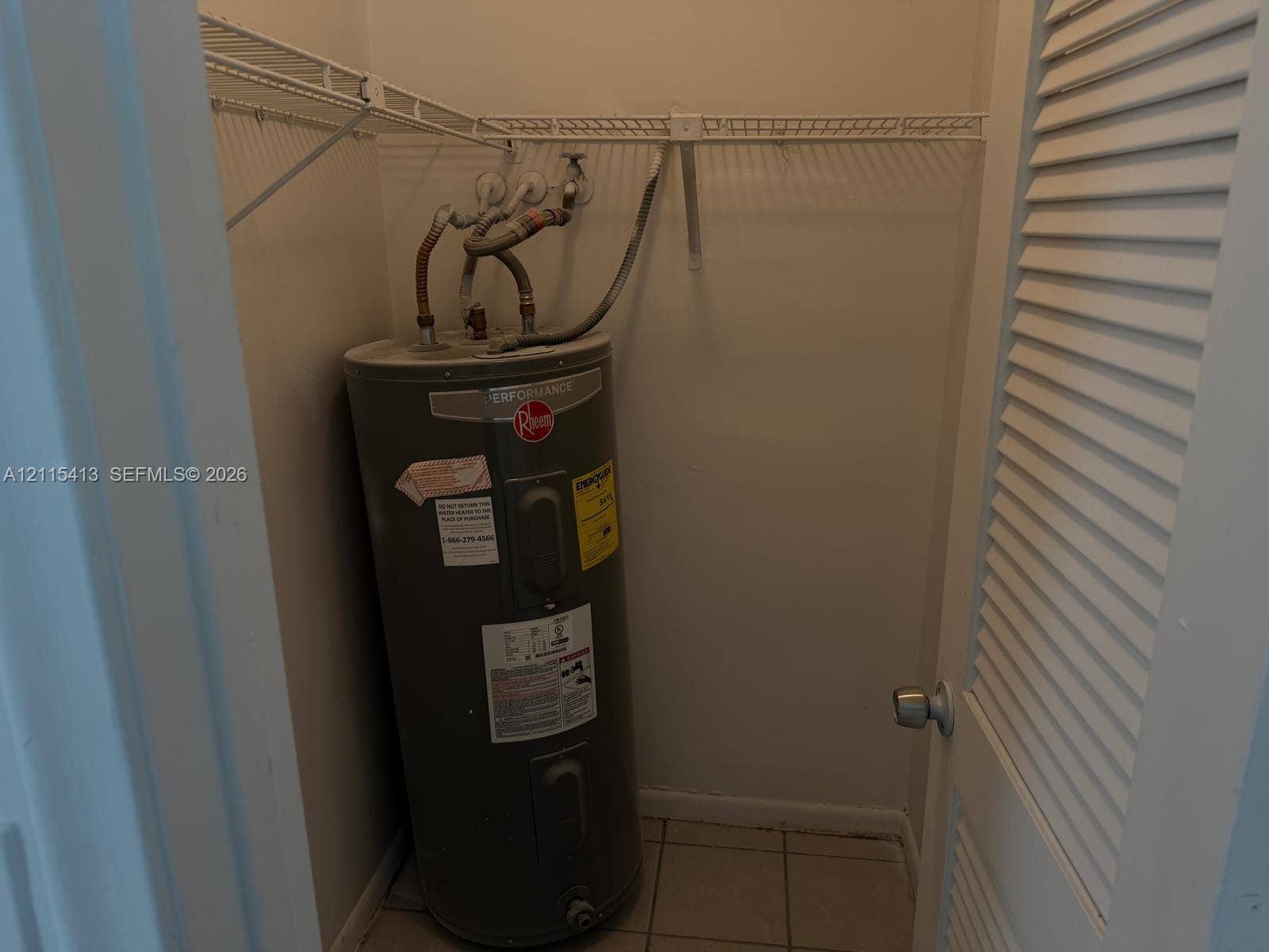 3001 NW 4th Terrace, #173, Pompano Beach, Pompano Beach, FL 33064 Utility closet featuring a water heater, tiled flooring, and overhead wire shelving behind a louvered door