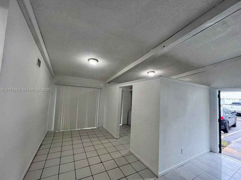 3001 NW 4th Terrace, #173, Pompano Beach, Pompano Beach, FL 33064 Interior space featuring neutral tile flooring, exposed ceiling beams, flush-mount lighting, and vertical sliding glass doors