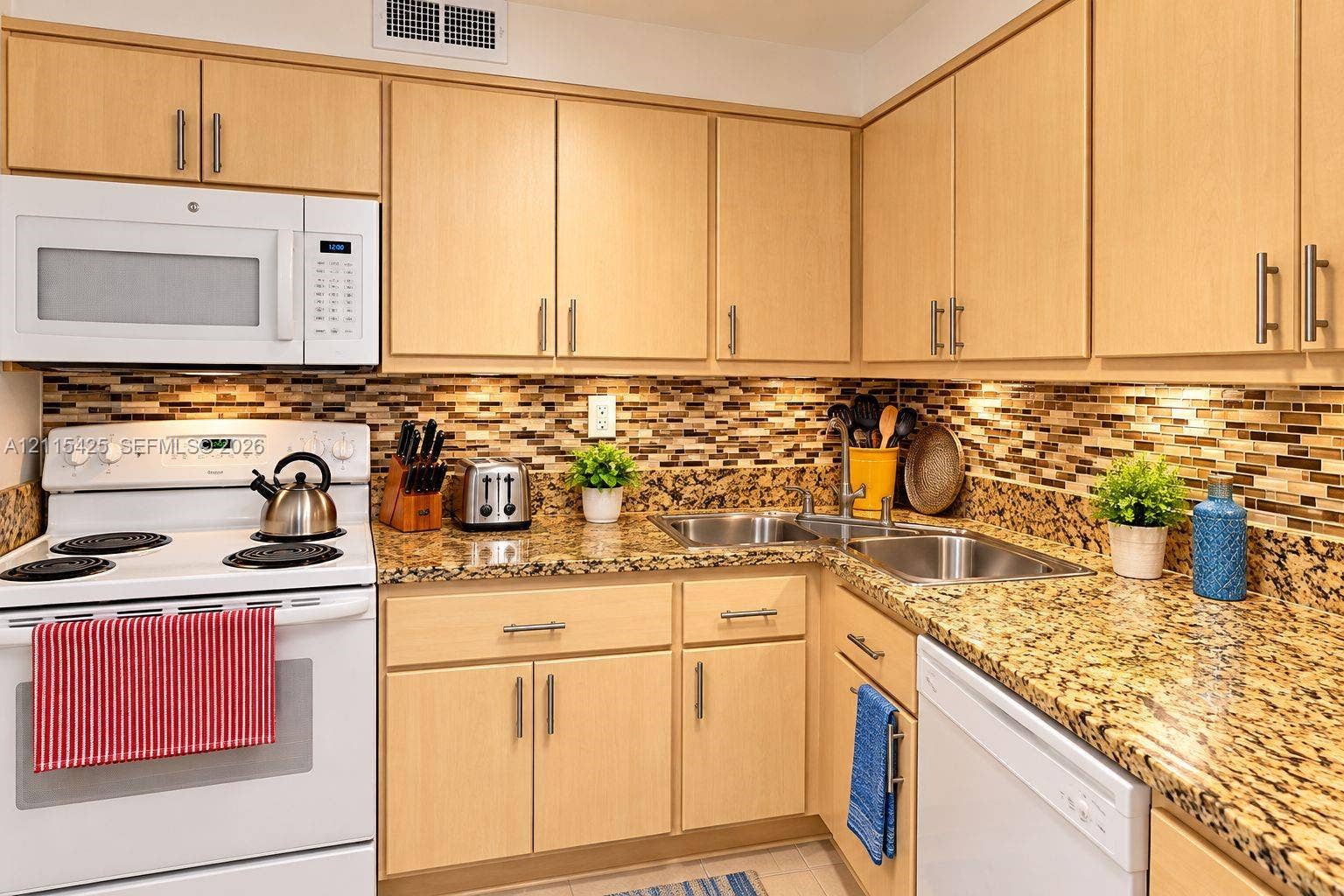 550 Bayshore Drive, #404, Fort Lauderdale, FL 33304 Kitchen featuring light-finish cabinetry with silver-tone hardware, speckled stone-finish countertops, a multi-tonal glass tile backsplash, and stainless steel double-basin sink