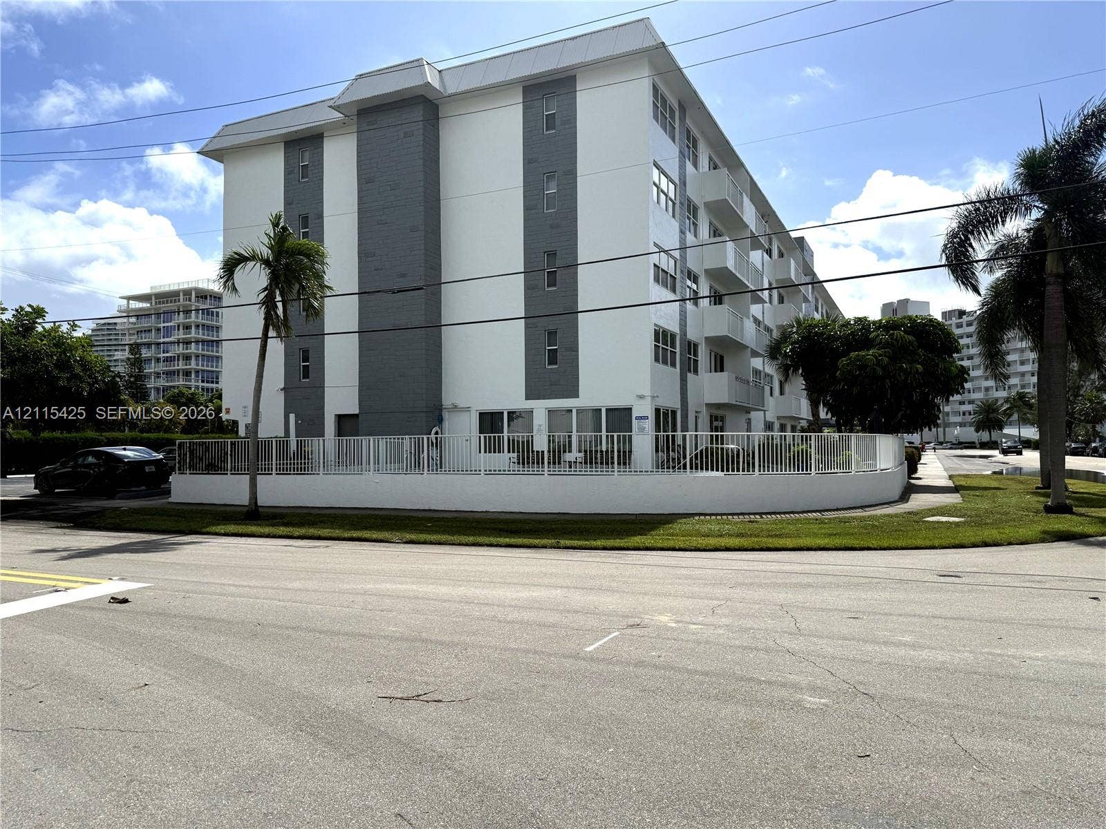 550 Bayshore Drive, #404, Fort Lauderdale, FL 33304 Multi-story building featuring white stucco exterior, grey paneled accents, private balconies, and a perimeter fence enclosing the property grounds