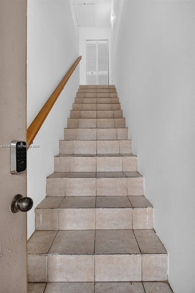 503 Gardens Drive, #201, Pompano Beach, Pompano Beach, FL 33069 Staircase featuring tile treads, a wood-finish handrail, and white louvered-panel double doors