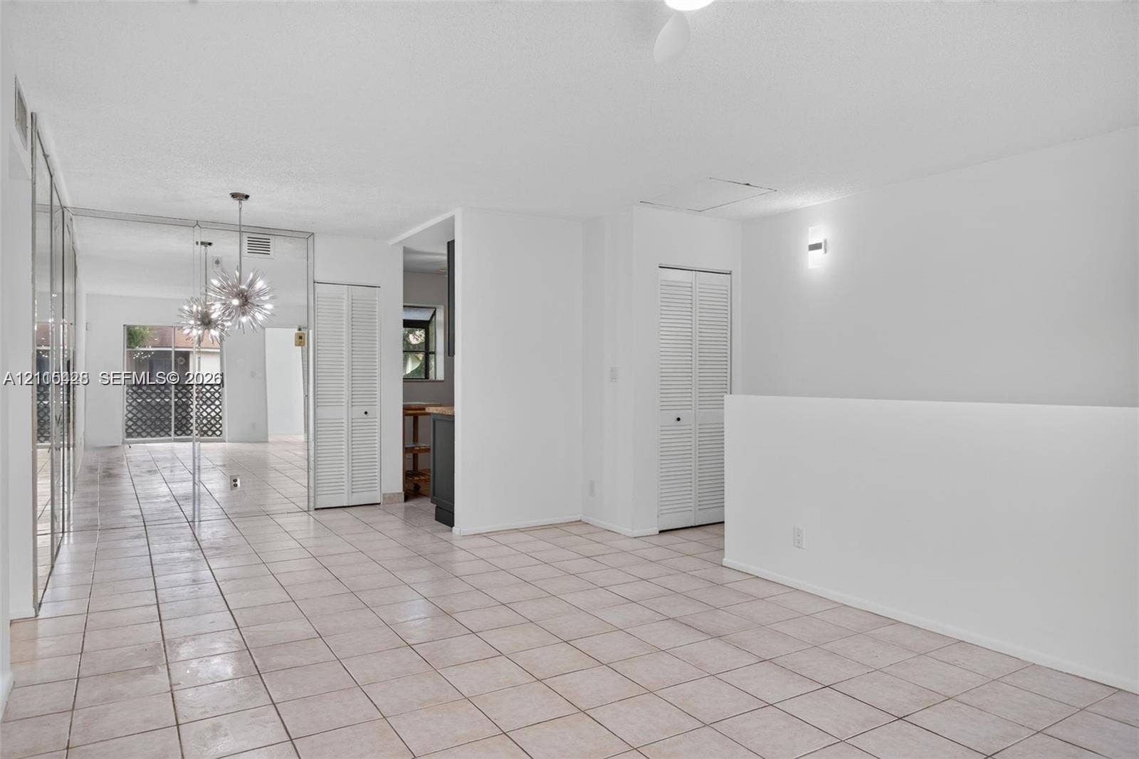 503 Gardens Drive, #201, Pompano Beach, Pompano Beach, FL 33069 Open-concept interior featuring light-toned tile flooring, floor-to-ceiling mirrored wall panels, louvered-door closets, and a decorative multi-bulb pendant fixture