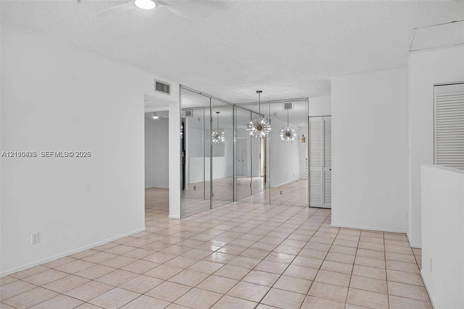 503 Gardens Drive, #201, Pompano Beach, Pompano Beach, FL 33069 Living area featuring neutral tile flooring, floor-to-ceiling mirrored closet doors, a ceiling fan with light fixture, and louvered bifold closet doors