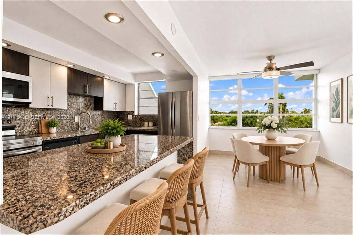 Kitchen featuring stone countertops, two-tone cabinetry, stainless steel appliances, recessed lighting, and large windows with exterior scenery