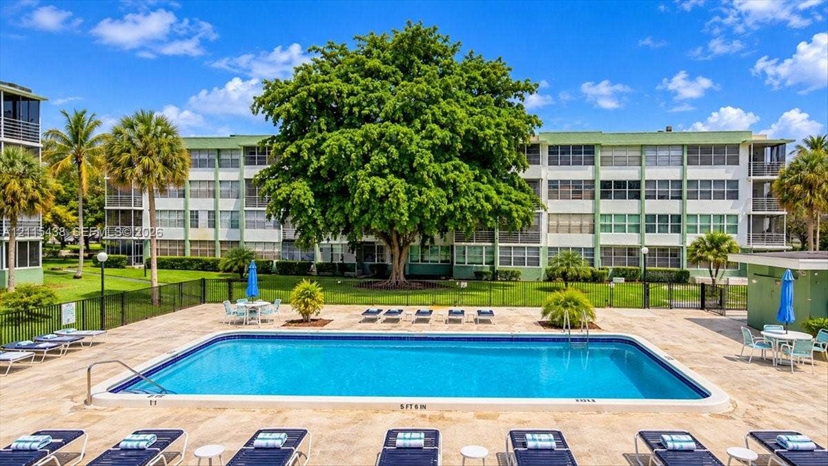 Swimming pool featuring a concrete deck, metal perimeter fencing, and mature landscaping