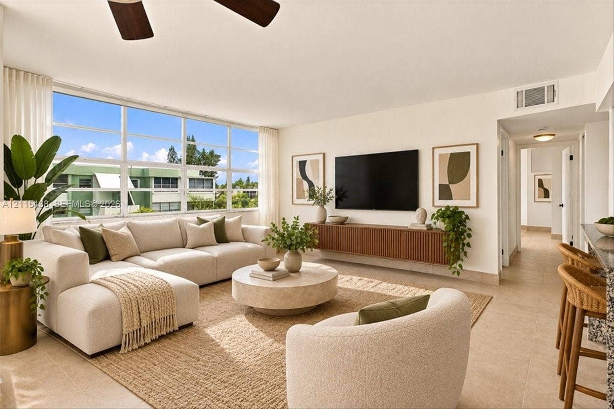 Living area featuring expansive floor-to-ceiling windows, neutral tile flooring, a wall-mounted floating wood-finish media console, and an integrated ceiling fan