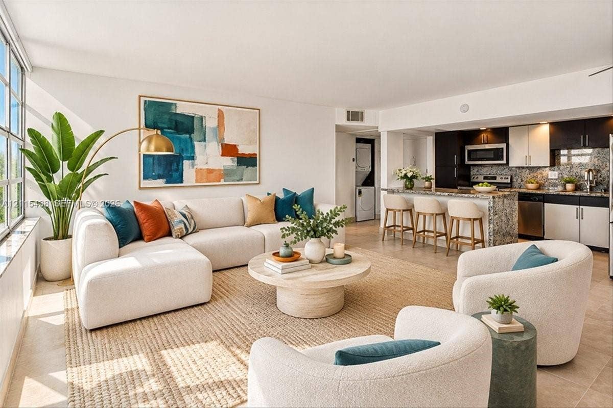 Open-concept kitchen featuring two-tone cabinetry, stone-surfaced island with breakfast bar seating, stainless steel appliances, and large-format floor tiling