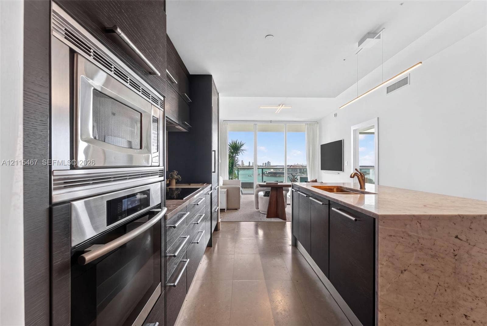 900 Biscayne Boulevard, #2104, Miami, FL 33132 Kitchen featuring dark cabinetry, stone-topped island with integrated sink, stainless steel wall oven and microwave, and linear pendant lighting