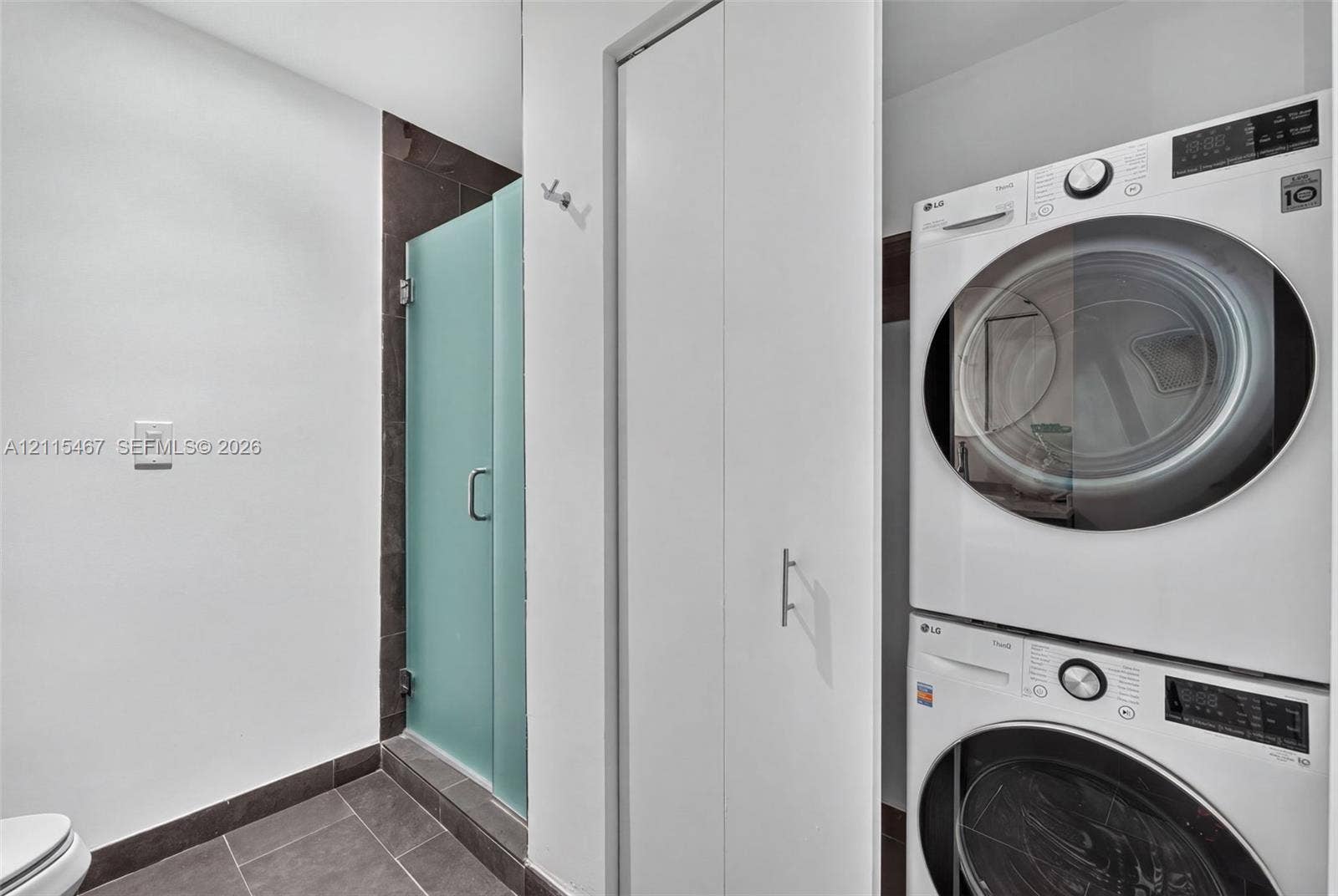 900 Biscayne Boulevard, #2104, Miami, FL 33132 Stacked front-load laundry unit, walk-in shower with a frosted glass door, dark tile flooring, and integrated wall cabinetry
