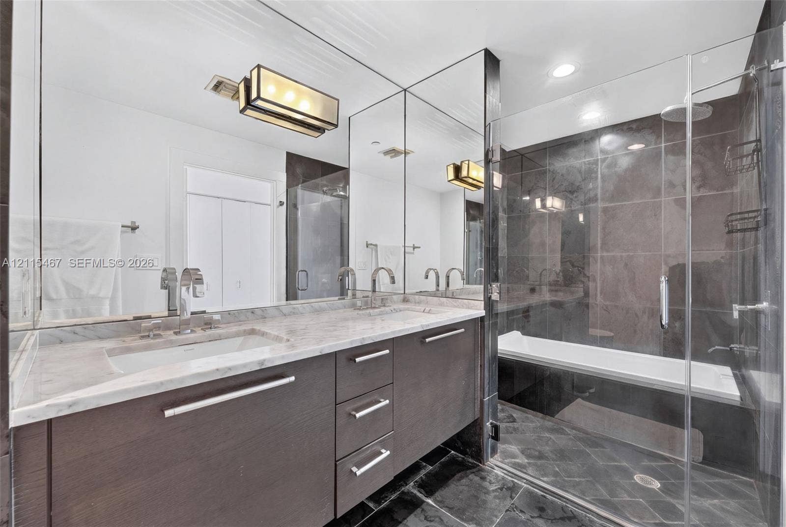 900 Biscayne Boulevard, #2104, Miami, FL 33132 Bathroom featuring a stone-topped vanity with double integrated sinks, dark wood-finish cabinetry, full-width wall mirror, and a glass-enclosed bathtub with large-format tile surround
