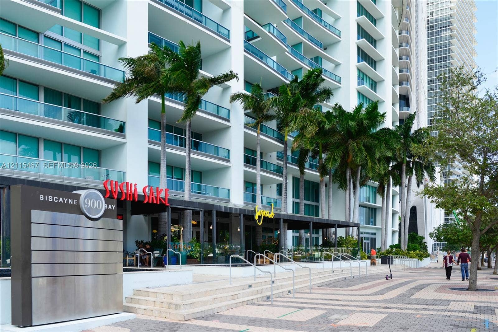 900 Biscayne Boulevard, #2104, Miami, FL 33132 High-rise facade featuring glass-railed balconies and ground-level commercial frontage with stone staircases and palm tree landscaping