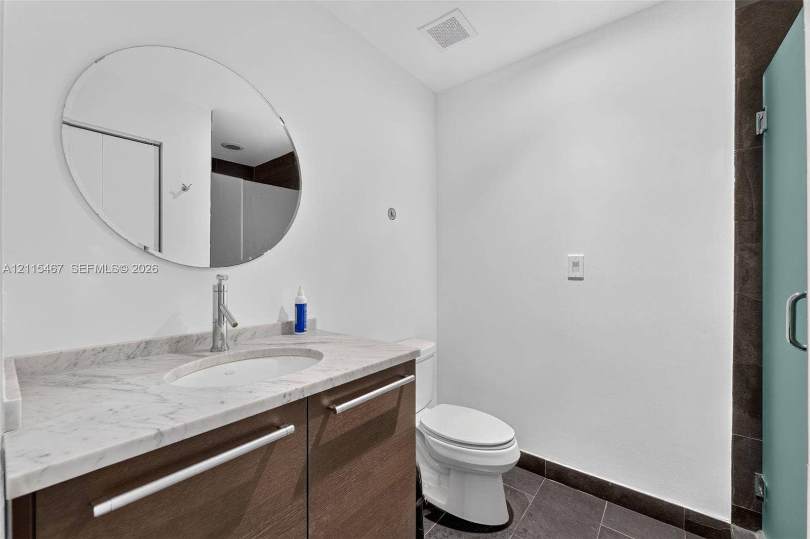 900 Biscayne Boulevard, #2104, Miami, FL 33132 Floating vanity with a stone countertop, oval undermount sink, and polished metal faucet, complemented by a circular wall mirror and dark tile flooring