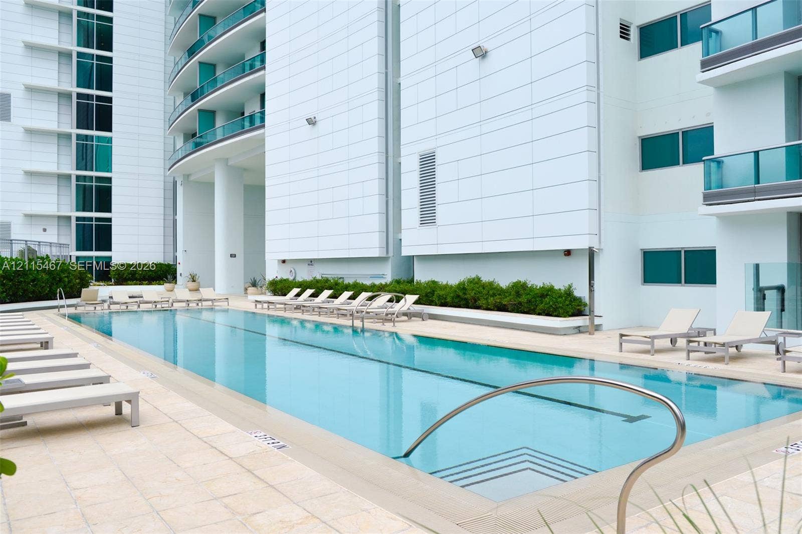 900 Biscayne Boulevard, #2104, Miami, FL 33132 Rectangular lap pool featuring stone-tile decking, integrated entry steps, stainless steel handrails, and surrounding manicured hedging