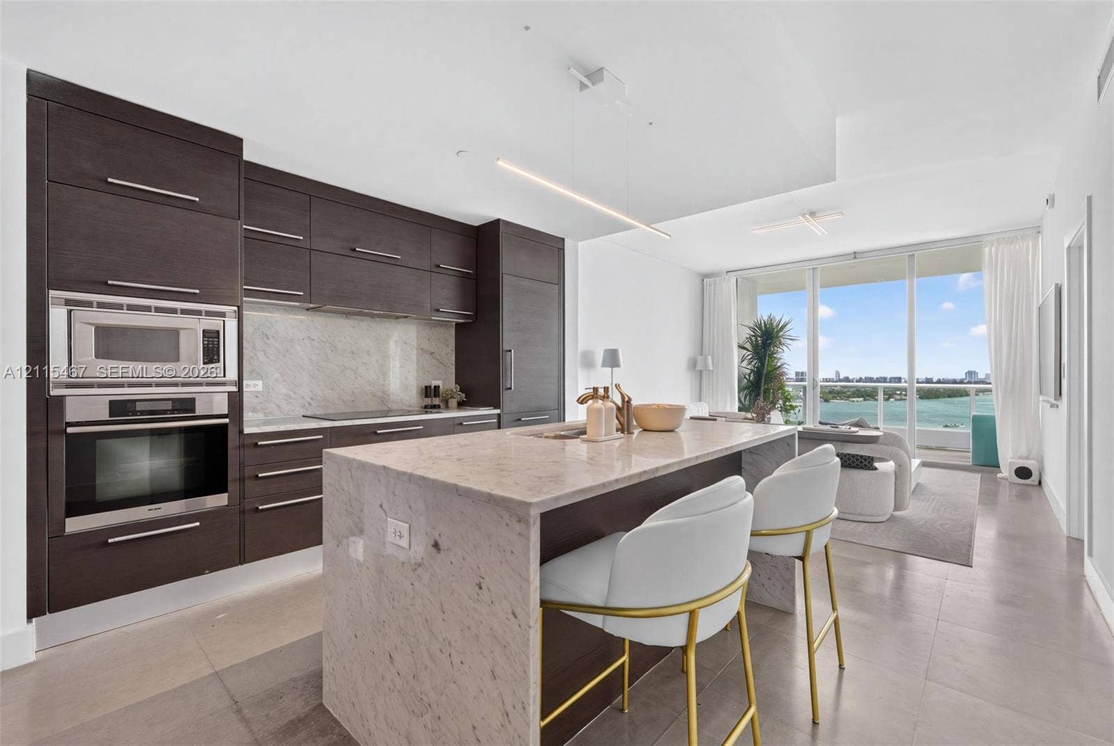 900 Biscayne Boulevard, #2104, Miami, FL 33132 Modern kitchen featuring flat-panel cabinetry, stone countertops, integrated stainless steel appliances, a waterfall-edge island, and floor-to-ceiling glass doors