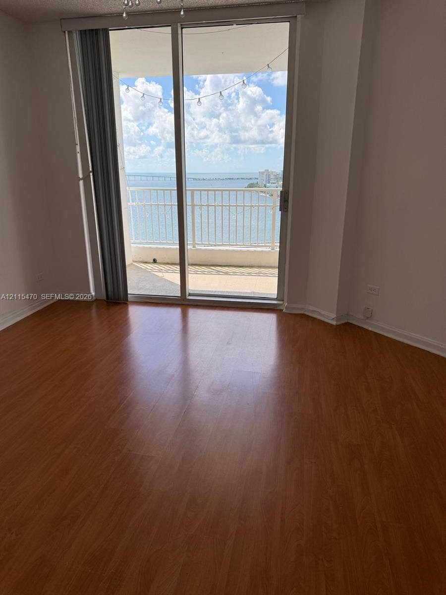 Wood-finish flooring, sliding glass door, and covered balcony with metal railing overlooking the water