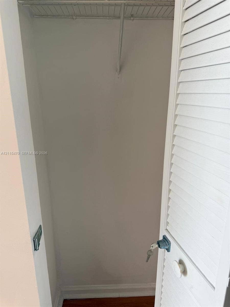 Storage closet featuring a white louvered door, a built-in wire shelf, a metal hanging rod, and a locking knob