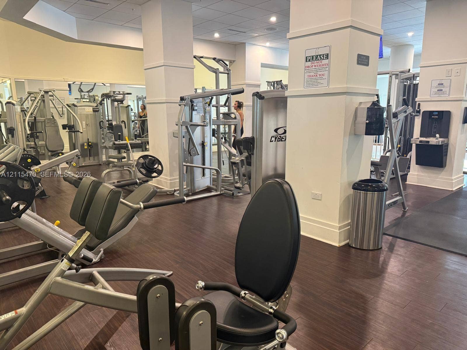 Fitness center featuring wood-finish flooring, structural columns, wall-mounted water dispenser, and multi-station exercise equipment