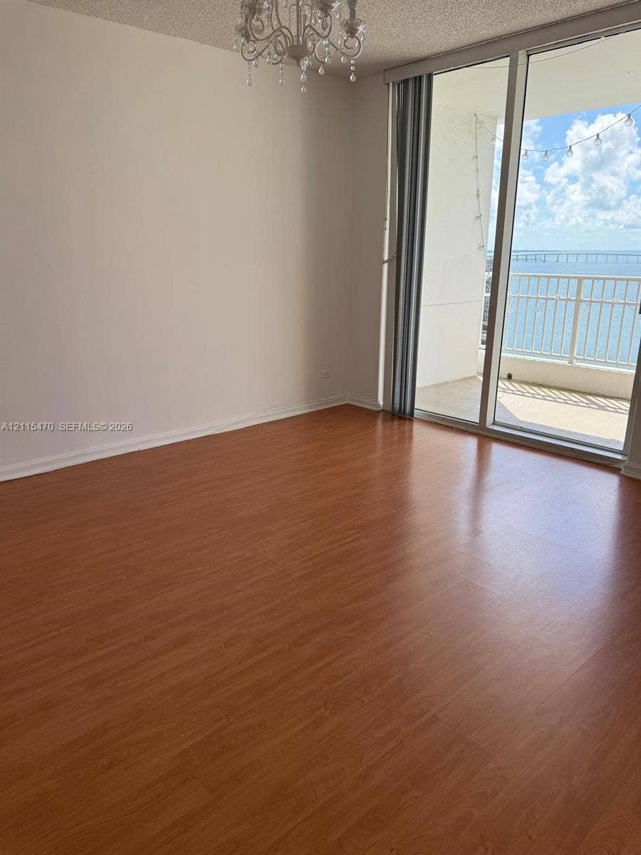 Wood-finish flooring, floor-to-ceiling glass doors, private balcony, and decorative chandelier