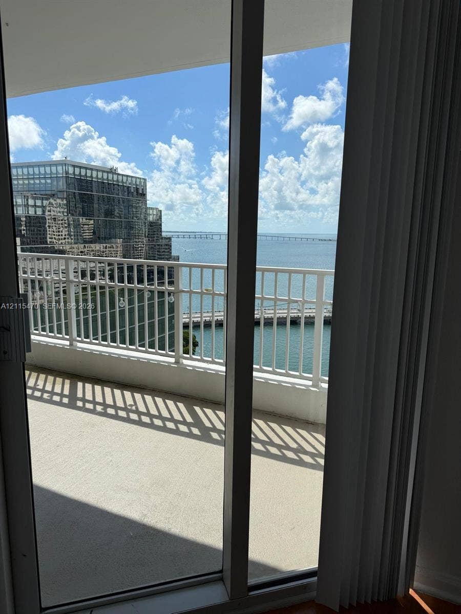 Private balcony with white metal railing, floor-to-ceiling glass sliding door, and water scenery
