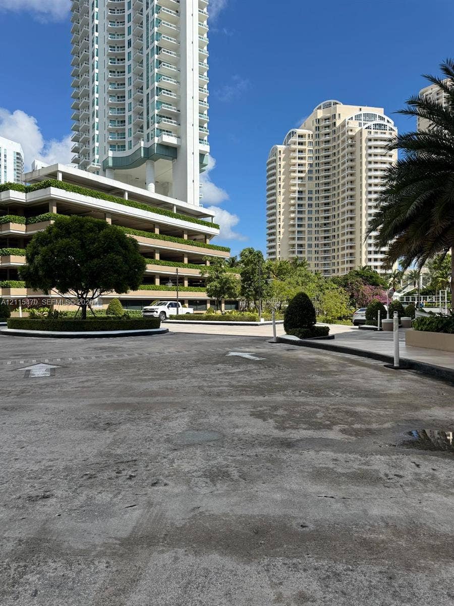 Asphalt motor court featuring landscaped greenery, mature trees, and high-rise building exteriors