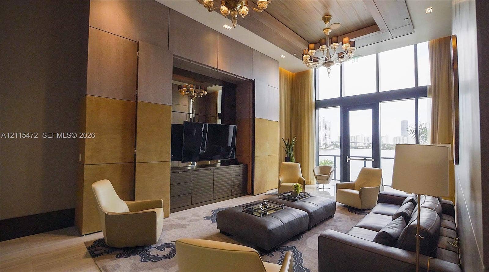 Double-height ceiling with wood paneling, floor-to-ceiling windows, custom built-in cabinetry, and ornate multi-tiered chandeliers