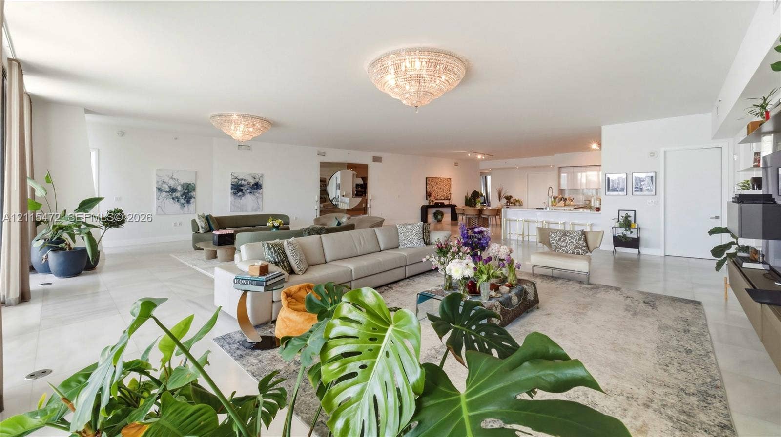 Open-concept living space featuring large-format tile flooring, recessed lighting, ornate crystal flush-mount chandeliers, and a kitchen island with stone-finish countertops