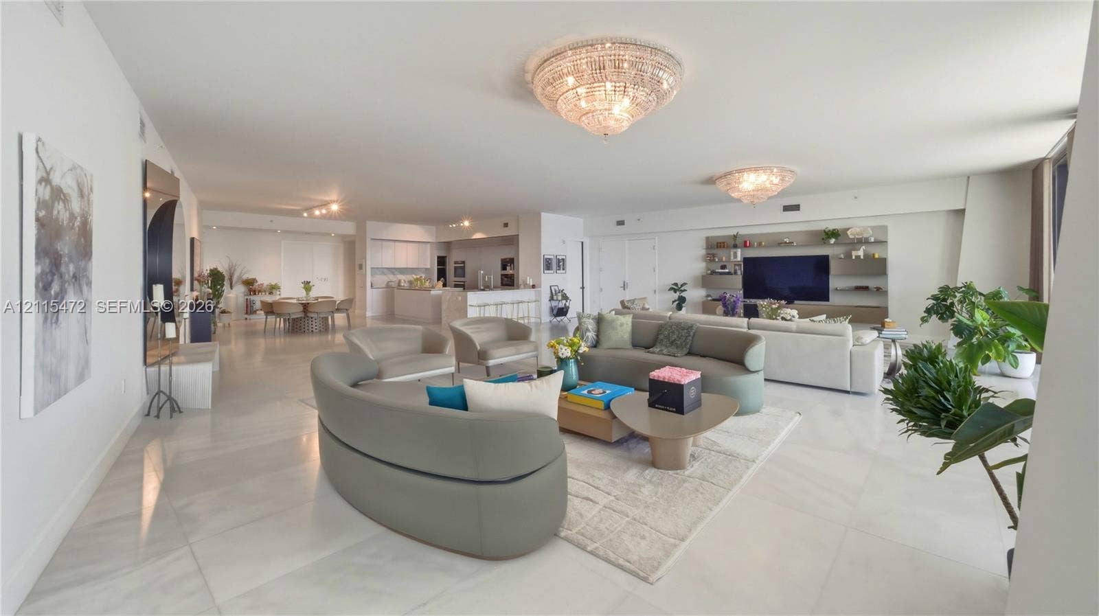 Open-concept living space featuring large-format tile flooring, dual crystal chandeliers, and custom wall-integrated cabinetry