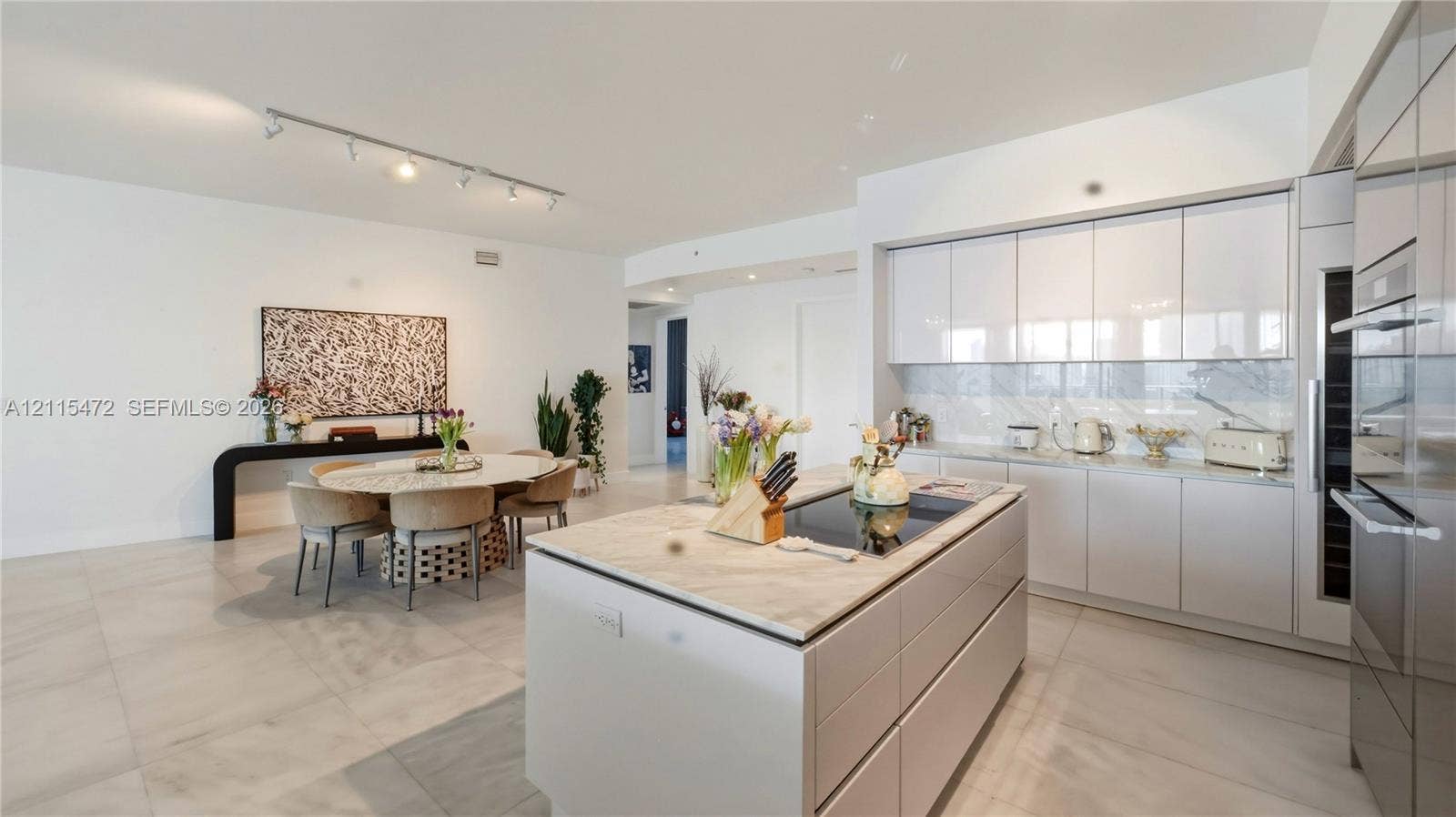 Modern kitchen featuring high-gloss cabinetry, a stone-topped island with a cooktop, integrated stainless steel appliances, and large-format porcelain tile flooring