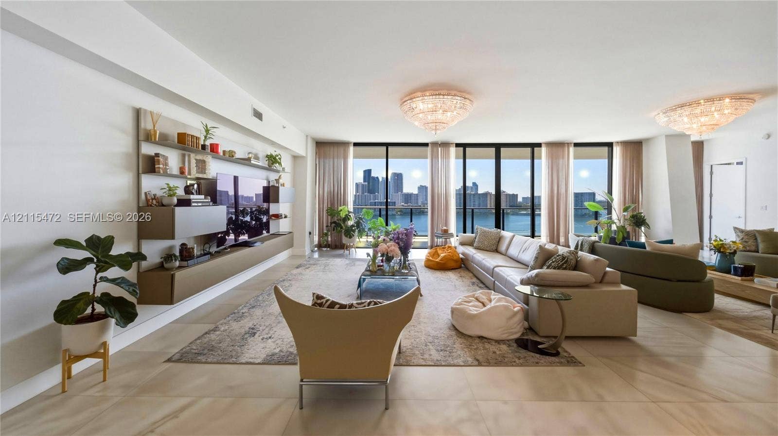 Open-concept living space featuring expansive floor-to-ceiling windows, integrated wall-mounted cabinetry, polished stone flooring, and dual tiered crystal flush-mount lighting fixtures