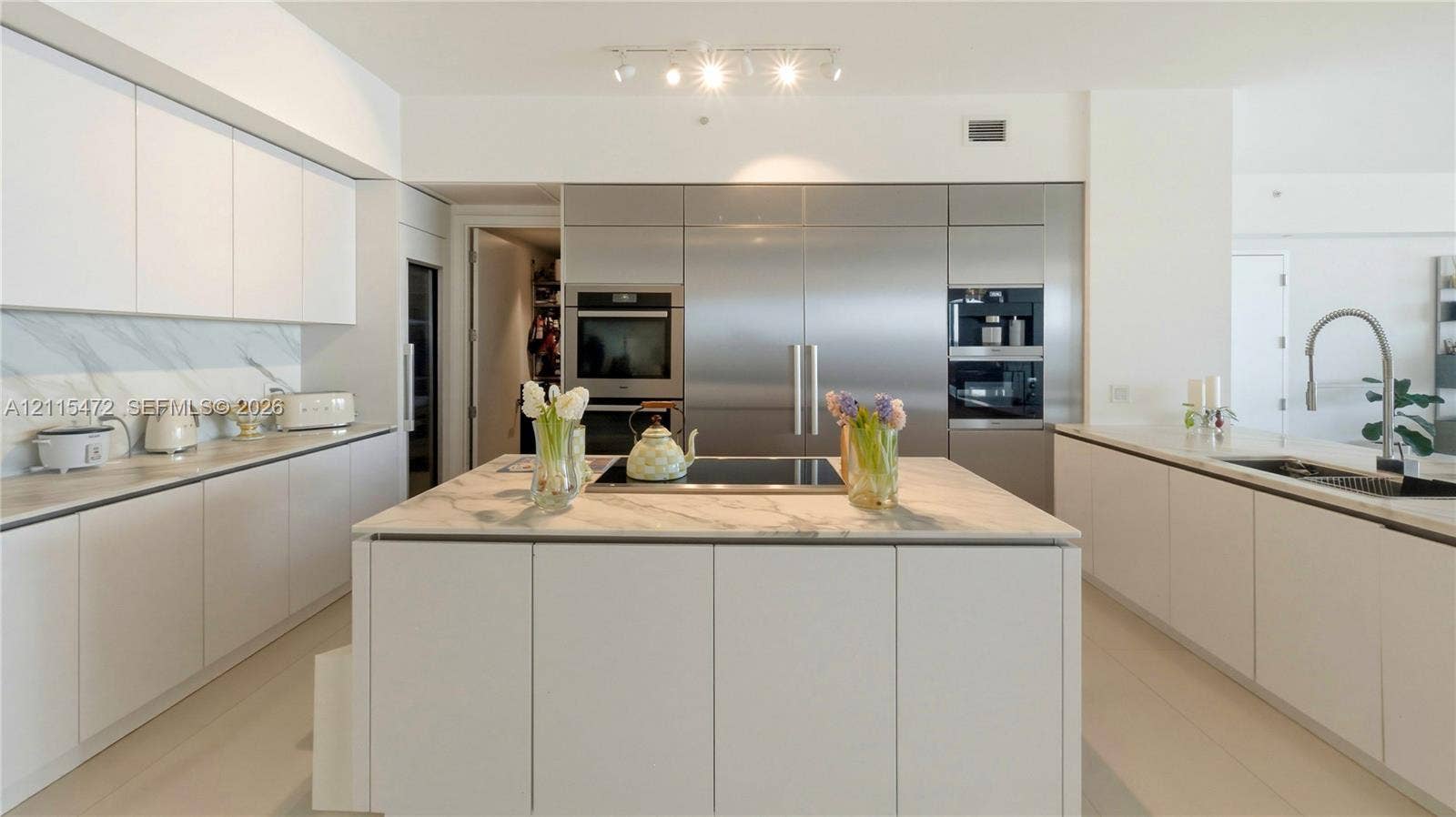Modern kitchen featuring custom flat-panel cabinetry, integrated stainless steel appliances, a center island with a stone countertop, stone-patterned backsplash, and polished faucet fixtures