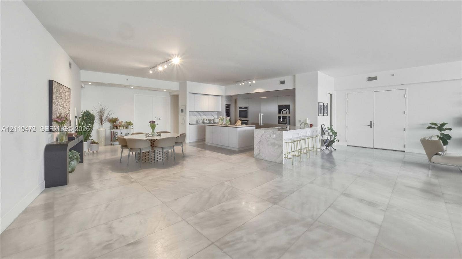 Large-format stone tile flooring, central kitchen island with stone waterfall countertop, flat-panel cabinetry, and built-in wall ovens