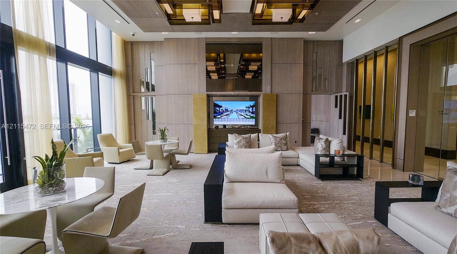 Floor-to-ceiling windows, wood-paneled wall treatments, recessed ceiling lighting with geometric fixtures, and integrated built-in media center