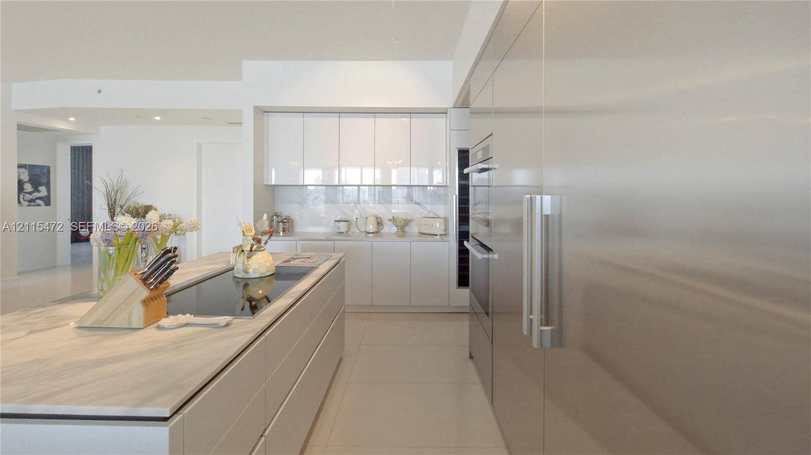 Kitchen featuring a central island with a stone-finish countertop and built-in cooktop, high-gloss flat-panel cabinetry, integrated stainless steel appliances, and large-format tile flooring