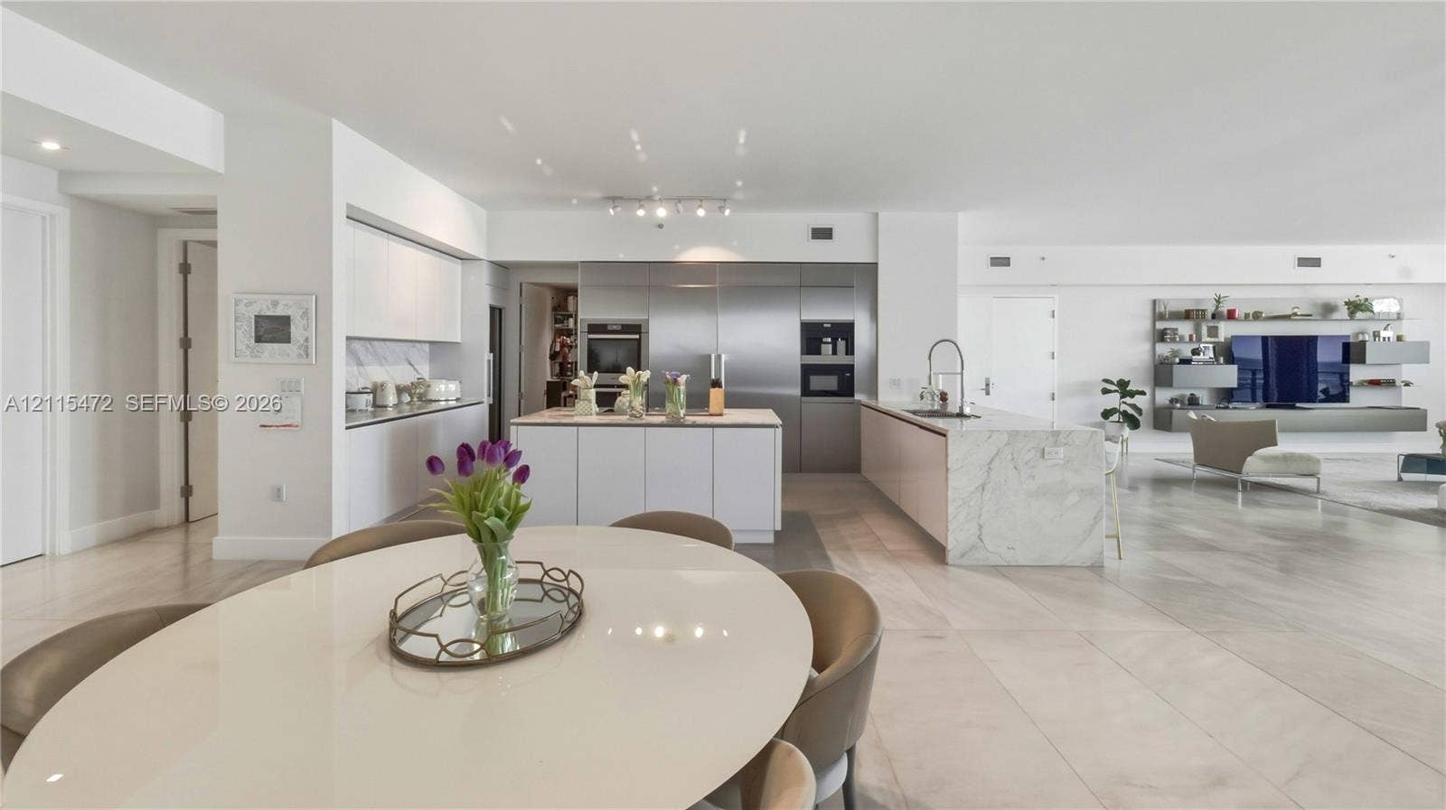 Modern kitchen featuring white flat-panel cabinetry, stone waterfall-edge island, integrated stainless steel appliances, and large-format tile flooring