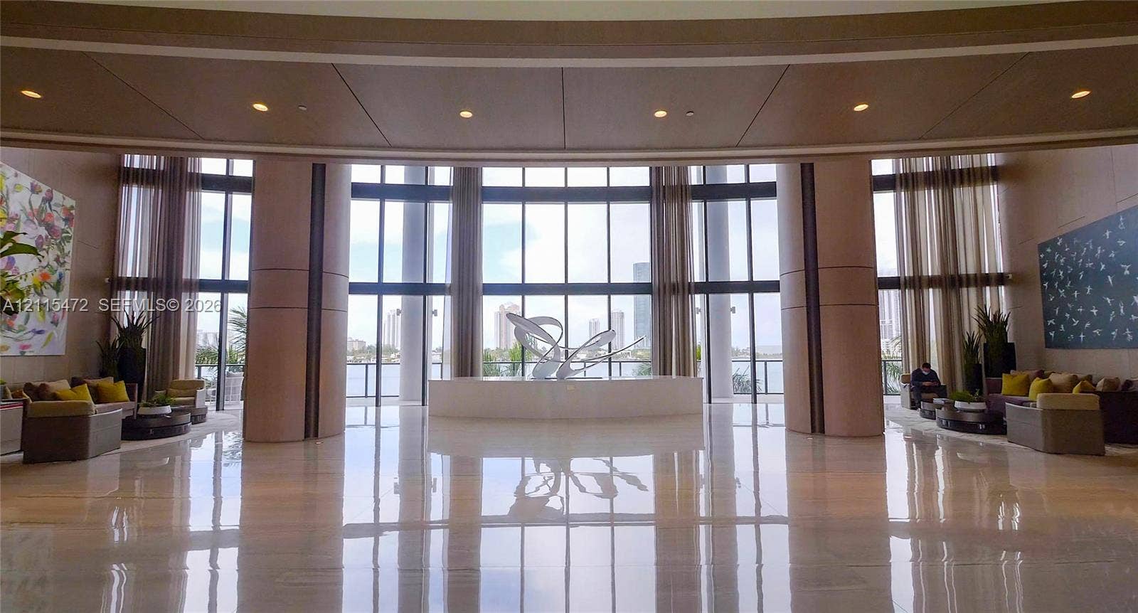 Grand lobby featuring expansive floor-to-ceiling windows, polished stone flooring, recessed ceiling lighting, and large structural support columns