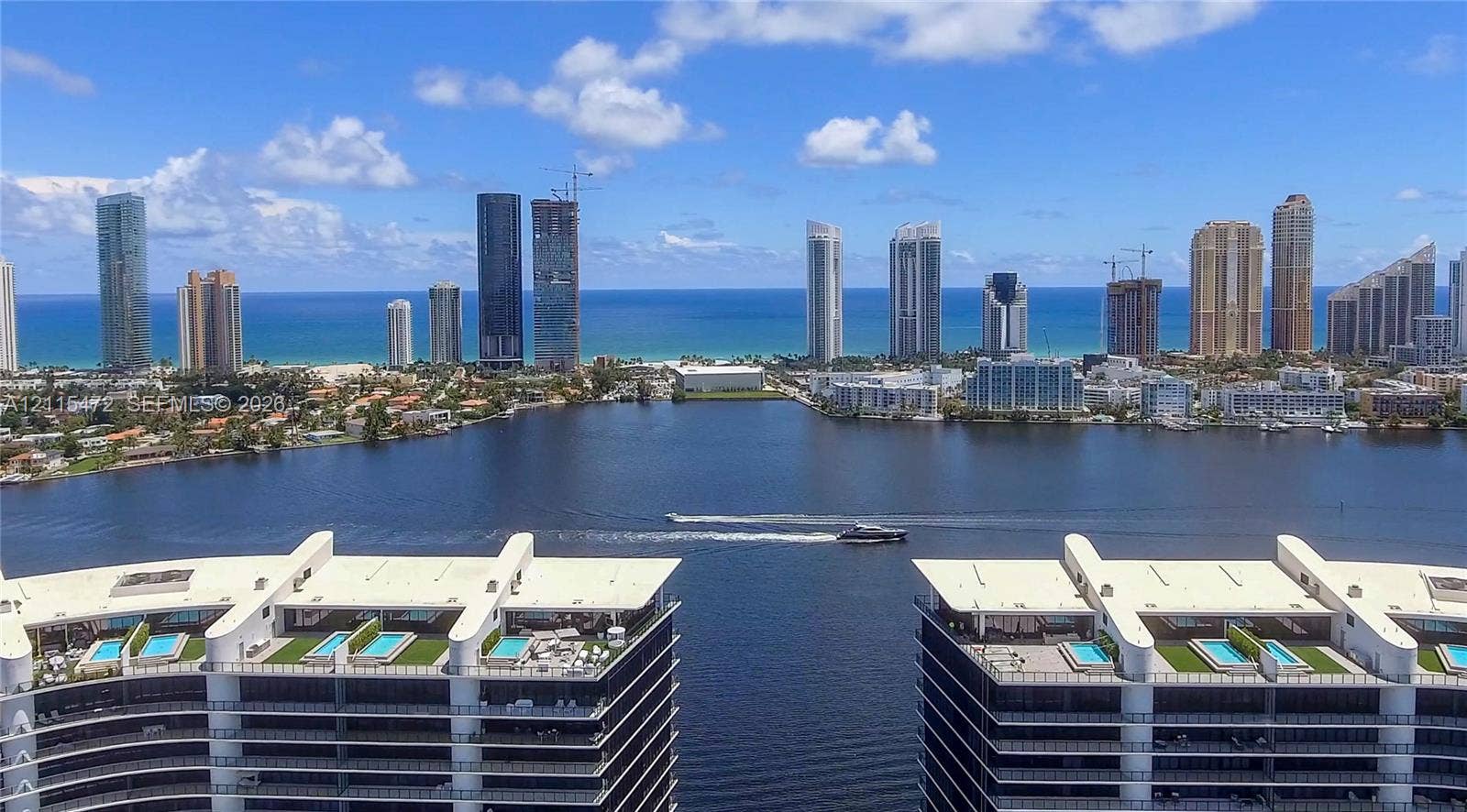 High-rise residential buildings featuring rooftop terraces, private plunge pools, and balcony landscaping, overlooking an expansive waterway and coastal skyline