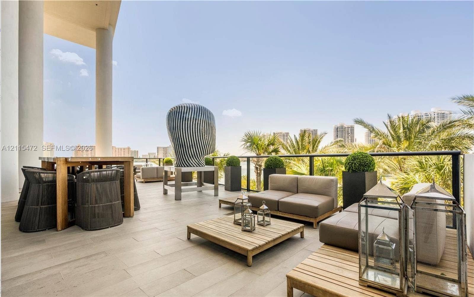 Expansive covered terrace featuring large-format stone-finish tile flooring, structural columns, and a perimeter railing with black metal framing